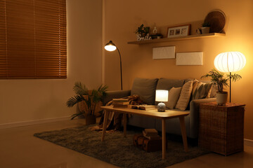 Interior of dark living room with glowing lamps, sofa and table at night