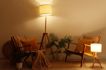 Interior of living room with glowing lamps, armchairs and palm plants at night