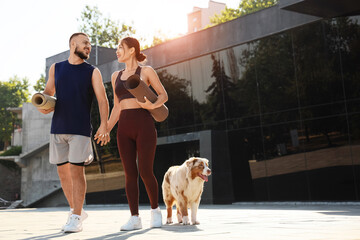 Sporty young couple with fitness mats and Australian Shepherd dog outdoors