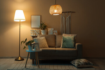Interior of dark living room with glowing lamps, sofa and tables at night
