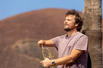 One handed trumpet player preparing his instrument near a palm tree
