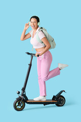 Female African-American student in headphones riding electric scooter on blue background