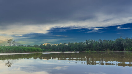 Morning in the jungle. A tourist motorboat is sailing on a calm river. Thickets of rain forest trees on the shore. Blue sky, clouds. Reflection on the smooth shiny surface of the water. Malaysia. 