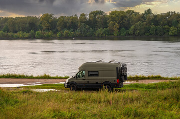 Fototapeta premium Camping on nature. Caravan recreational vehicle on the riverbank at sunset after summer rain.