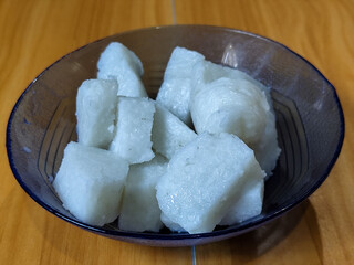 The lontong pieces are served in a glass bowl, placed on a wooden table.