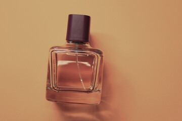 ​A transparent perfume bottle with a dark purple cap lying on a solid beige background. The...