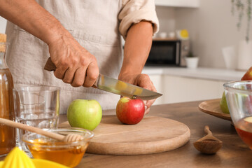 Mature man cutting apple for cider in kitchen, closeup
