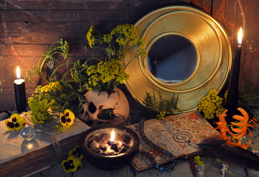Mystic still life with skull, mirror, decorated magic book of spells, tansy flowers, black candles and witchy ritual objects.  No foreign language, only fantasy symbols