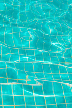 swimming pool water backgound with blue square tiles on floor distorted pattern by sun light and waves