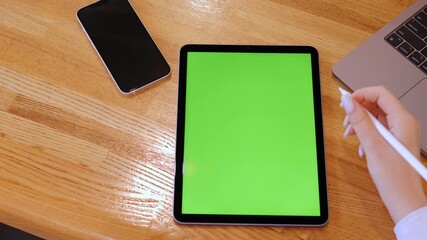Person is writing on a green tablet. A phone is on the table next to the tablet
