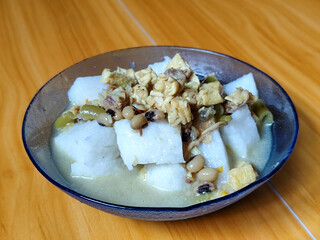 A bowl of vegetable rice cakes. Lontong vegetable in coconut milk sauce with tofu, beef which is a typical Indonesian food. Served on a wooden table.