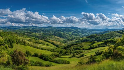 Panoramic view of rolling green hills and valleys under a vibrant blue sky dotted with fluffy cumulus clouds.  Sunlight illuminates the lush landscape