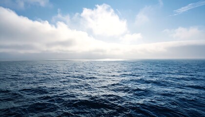 Vast oceanic expanse under a bright sky filled with drifting billowy clouds and soft atmospheric