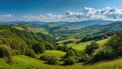 Fototapeta premium Panoramic view of rolling green hills and valleys under a vibrant blue sky with fluffy white clouds. Lush vegetation covers the landscape, showcasing a serene and idyllic countryside scene