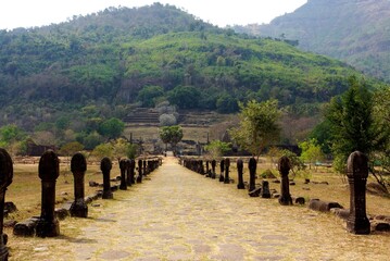 Ancient stone pathway leading to Wat Phou temple with lush green hills in the background