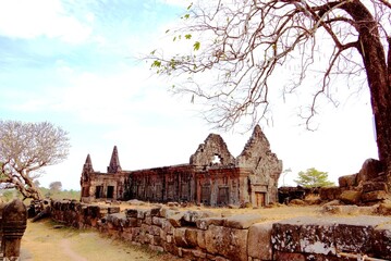 Ancient stone temple ruins of Wat Phou in Champasak, Laos, with a bare tree under a bright sky.