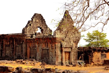 Ancient stone temple ruins of Wat Phou in Champasak, Laos, with a bare tree under a bright sky.