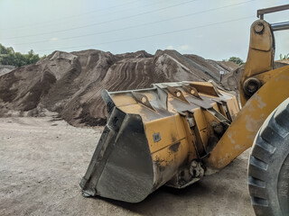 Yellow excavator with bucket attachment at a construction site, surrounded by dirt piles,...