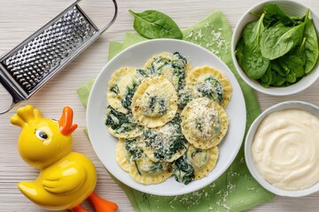Gourmet pasta with spinach, served on a plate with a creamy sauce.  A grater, fresh spinach, and a yellow duck are also visible