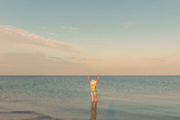 Woman with backpack standing in sea at sunset