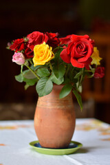 bouquet of colorful roses in the clay vintage vase at the table