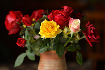 bouquet of colorful roses in the clay vintage vase at the table