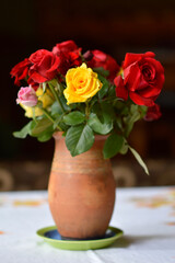 bouquet of colorful roses in the clay vintage vase at the table