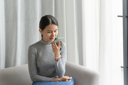 Asian woman using voice assistant on smartphone at home conversation with online assistant Voice chat bot conversational AI Modern Technologies.