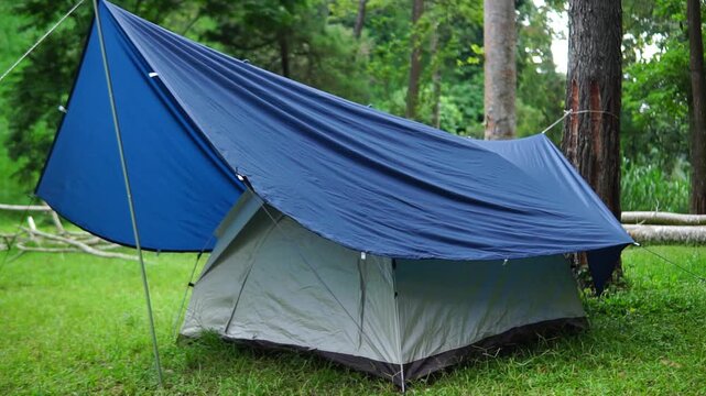 A camping tent equipped with a tarp flysheet for extra protection from the elements. Located in a beautiful camping area with a backdrop of shady trees.