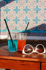 Close-up of two glasses with delicious cool cocktails on a table by the pool, sunglasses nearby. Summer drinks on vacation. 