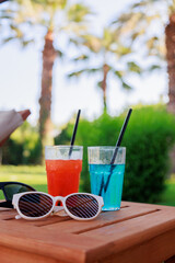 Close-up of two glasses with delicious cool cocktails on a table by the pool, sunglasses nearby....