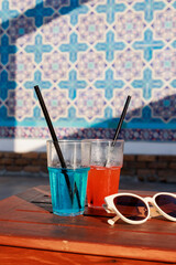 Close-up of two glasses with delicious cool cocktails on a table by the pool, sunglasses nearby....