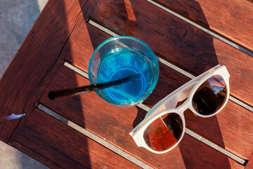 Close-up of a glass with a delicious cool cocktail on a table by the pool, sunglasses are lying nearby. Summer drinks on vacation 