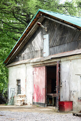 Old rustic barn standing in rural outdoor setting with weathered wooden roof, partially open red...