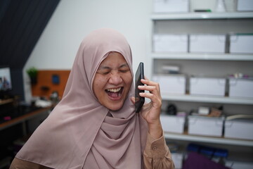 Happy smiling Asian muslim woman laughing when talking on phone, receiving good news