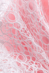 White lace with large circular openwork draped over soft pink background, evoking romance and...