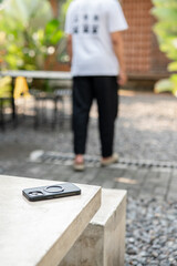 A man in a white shirt is walking past a table with a cell phone on it. The phone is an iPhone