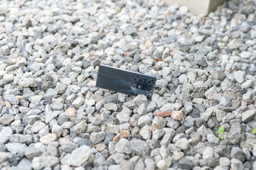 A cell phone is laying on the ground in a pile of rocks. The phone is cracked and broken