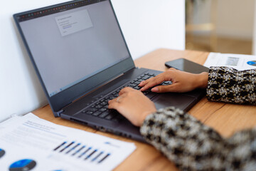 Person working on a laptop at a desk in an office setting. Screen displays documents, professional tasks, reading or editing files. Papers workspace organized for productivity.