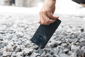 A black cell phone is being held by a person's hand. The phone is cracked and has a broken screen