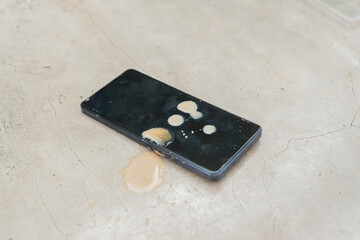 A cell phone is laying on a counter with a yellow substance on it. The phone is black and has a...