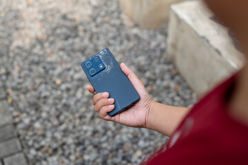 A person is holding a cell phone with a cracked screen. The phone is black and has a large screen