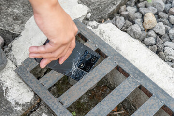 A person is holding a cell phone in their hand. The phone is black and has a cracked screen