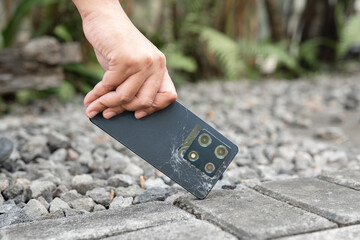 A person is holding a cell phone in their hand. The phone is black and has a cracked screen