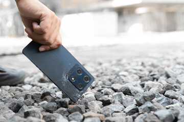 A person is holding a cell phone in their hand. The phone is black and has a cracked screen