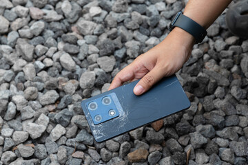 A person is holding a cell phone in their hand. The phone is black and has a cracked screen