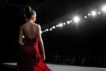 Fashion model strutting down the runway in a stunning red dress, captivating the audience during an exciting fashion show event