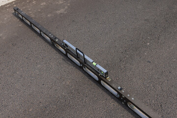 Measuring beam placed on asphalt road for surface inspection, close-up view.