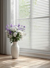 Fototapeta premium White vase of purple and white flowers sits on a light wood floor, beside a window with white blinds, sunlight streaming in