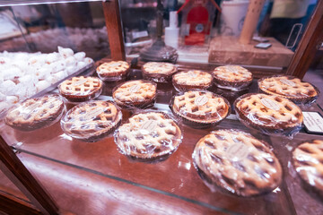 Beautiful handmade fruit pies with golden lattice pastry crusts showcased in illuminated glass display case at artisan bakery, perfect for food marketing and culinary business concepts.